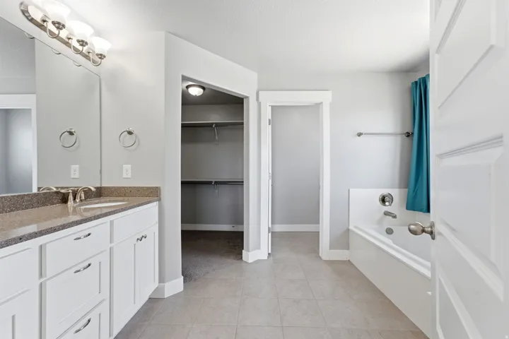 Bathroom featuring a dual vanity with a speckled countertop, undermount sinks, a built-in bathtub, and an adjacent walk-in closet