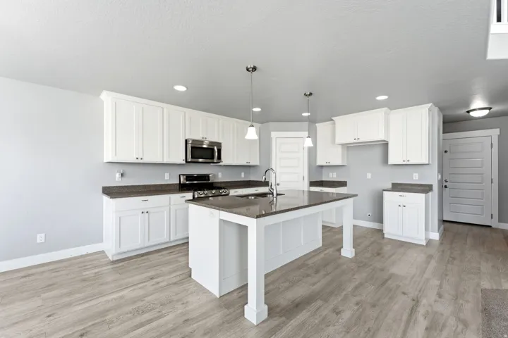 Kitchen featuring white shaker-style cabinetry, dark countertops, stainless steel appliances, a center island with pendant lighting, and wood-finish flooring
