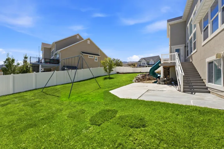 Expansive backyard featuring a manicured lawn, concrete patio, and white privacy fencing
