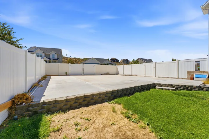 Expansive concrete pad, surrounded by a tall white privacy fence, with a retaining wall and a section of green lawn