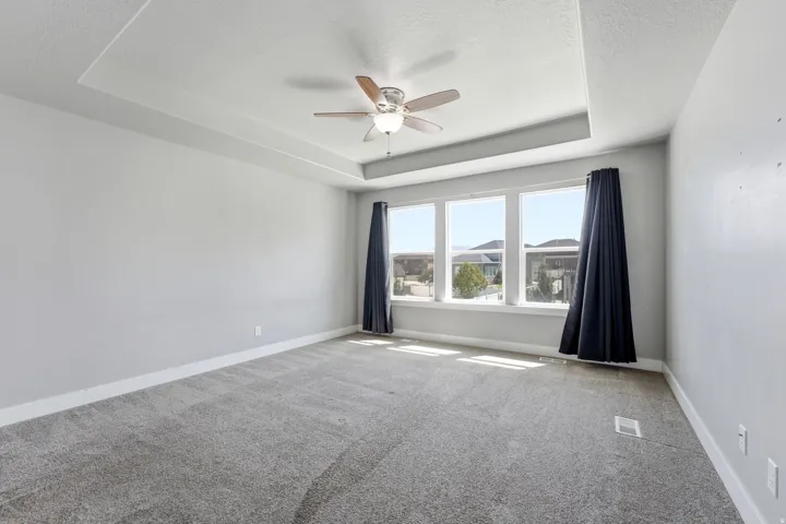 Tray ceiling with a ceiling fan, light-toned walls, gray carpet flooring, and multiple windows