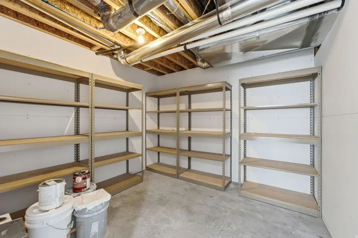Unfinished basement space featuring exposed ceiling joists, concrete flooring, and multiple built-in shelving units