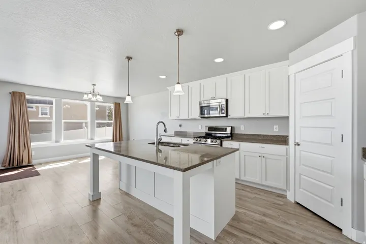 Kitchen featuring white cabinetry, a central island with a sink, recessed lighting, wood-finish flooring, and stainless steel appliances