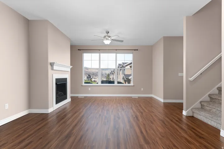 Spacious living area featuring wood-finish flooring, a white mantel fireplace, large picture window, and a ceiling fan with integrated lighting