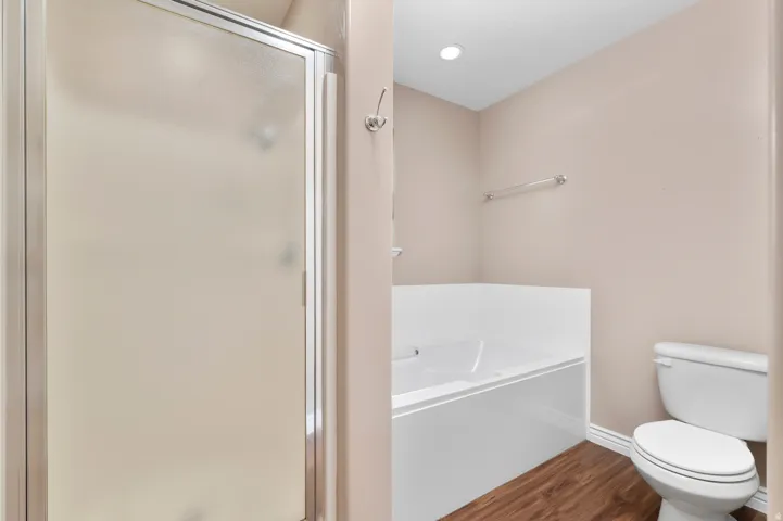 Frosted glass shower enclosure, built-in bathtub, toilet, wood-finish flooring, and recessed lighting