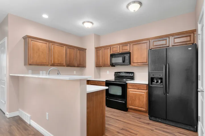Kitchen featuring wood-finish cabinetry, white countertops, black appliances, and wood-finish flooring