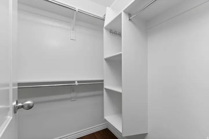 Walk-in closet with multiple hanging rods, built-in shelving, and wood-finish flooring