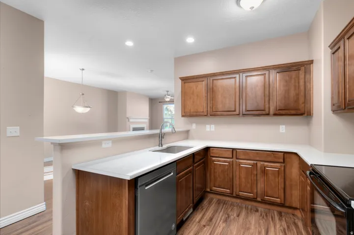 Kitchen featuring wood-finish flooring, wood cabinetry, stainless steel dishwasher, and light-toned countertops