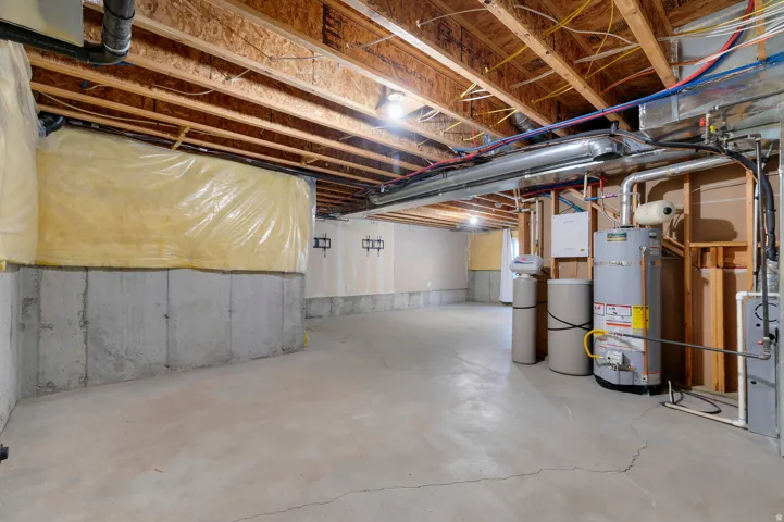 Unfinished basement featuring concrete flooring, exposed ceiling joists, and a water heater