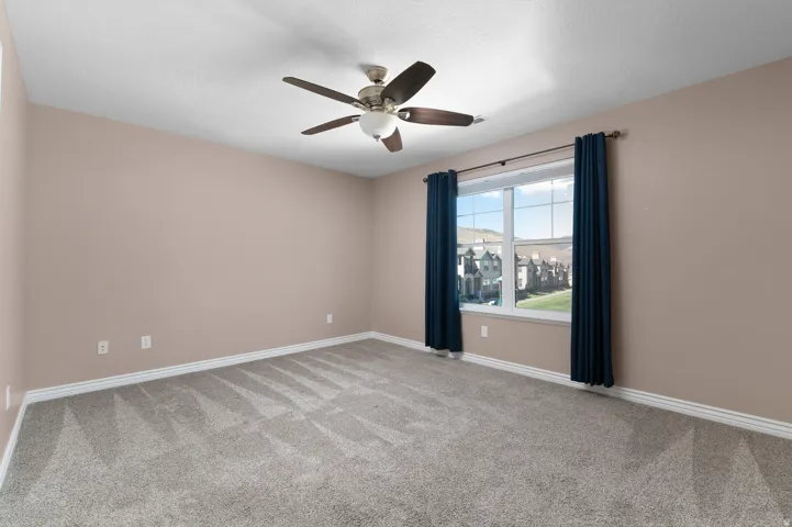 Spacious room with neutral wall color, grey patterned carpet, and a ceiling fan with integrated lighting