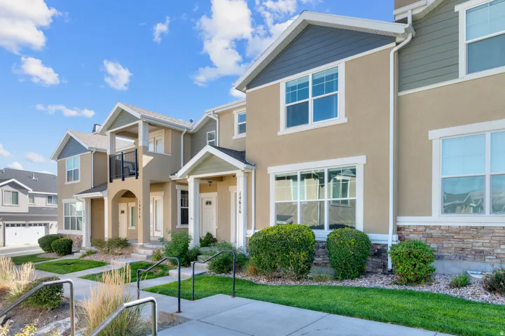 Multi-level townhome featuring stucco and horizontal siding, stone veneer accents, and a dedicated balcony with a black metal railing