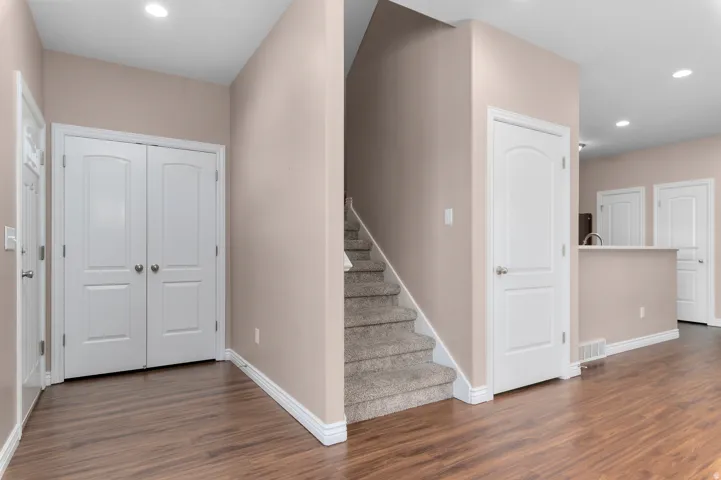 Wood-finish flooring, white trim, recessed lighting, and a staircase with carpeted treads