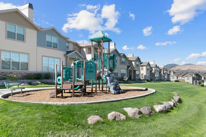 Expansive green space with a playground, wood chip surfacing, and a paved pathway