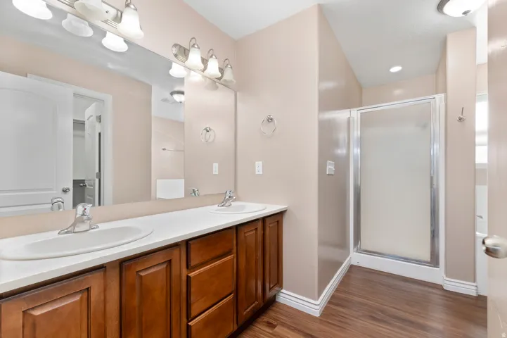 Dual sink vanity with wood-finish cabinetry, a white countertop, and an integrated shower enclosure