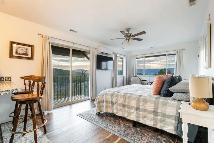 Sliding glass door access to an exterior balcony, wood-finish flooring, ceiling fan, and multiple windows