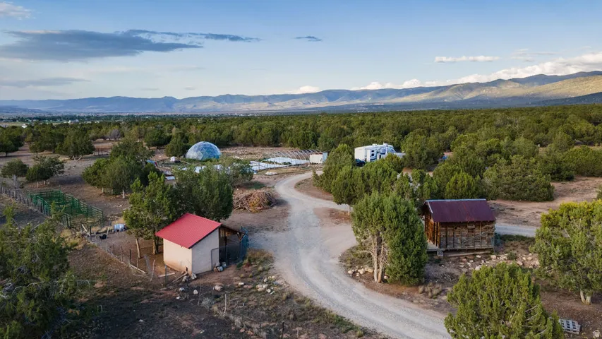 Sprawling property featuring multiple structures, including a geodesic dome, a shed with a red roof, and a rustic wood-sided cabin, all surrounded by abundant mature trees