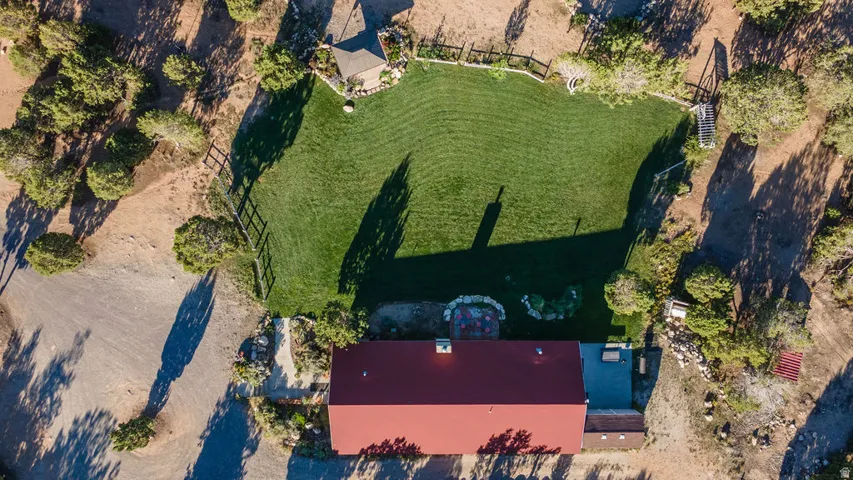 Expansive green lawn, fenced perimeter, surrounding natural landscaping, and red-roofed structure