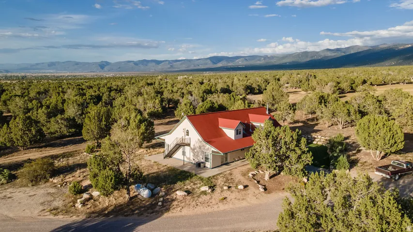Property featuring a red metal roof, dormer window, and exterior staircase, surrounded by extensive natural landscaping and distant mountains