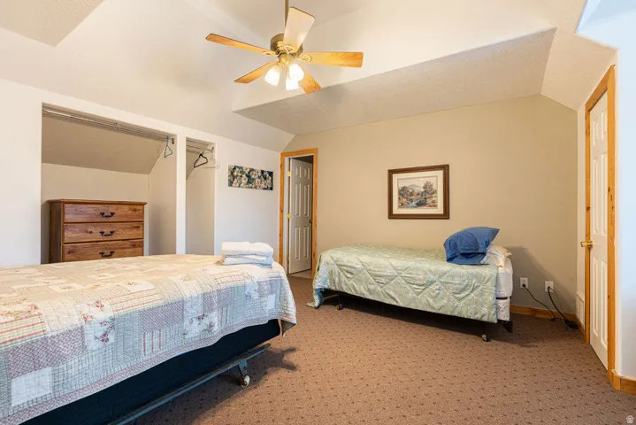 Carpeted flooring, vaulted ceiling, wood-finish ceiling fan, wood-finish trim, and an open closet