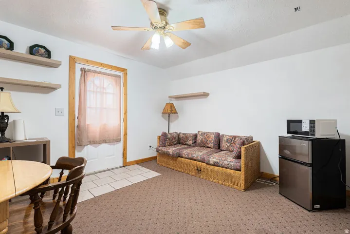 Carpeted flooring, ceiling fan with integrated lighting, wood-trimmed door, and floating wall shelves