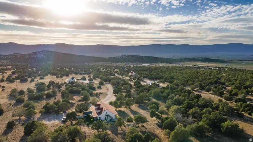 Expansive rural property with a detached residence featuring a red tile roof, surrounded by mature trees and a distant mountain range backdrop