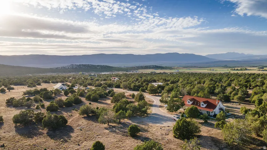 Expansive property featuring a residence with a red roof, a separate white structure, and a winding driveway, surrounded by abundant mature trees and distant mountain ranges