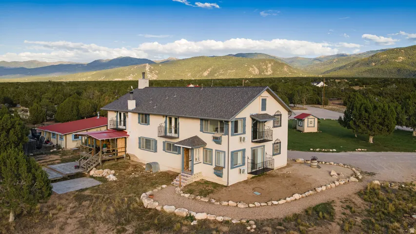 Two-story stucco exterior, multiple Juliette balconies, covered porch, detached auxiliary building, and a gravel driveway
