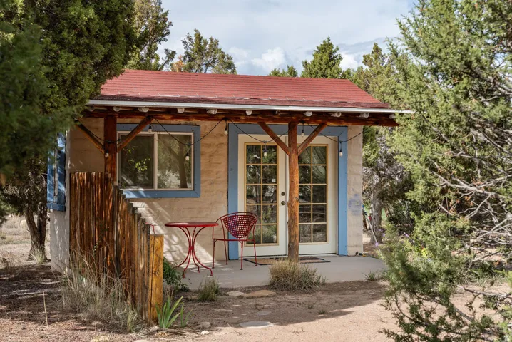 Attached covered porch with exposed wood beams, red corrugated metal roof, and double glass-paned doors