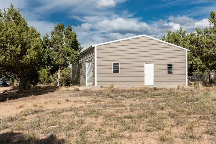 Metal-sided outbuilding featuring a white pedestrian door, two windows, and a roll-up garage door