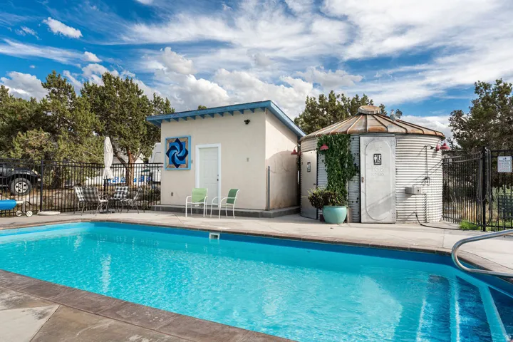 Expansive swimming pool with concrete decking, surrounding privacy fencing, and two adjacent outbuildings