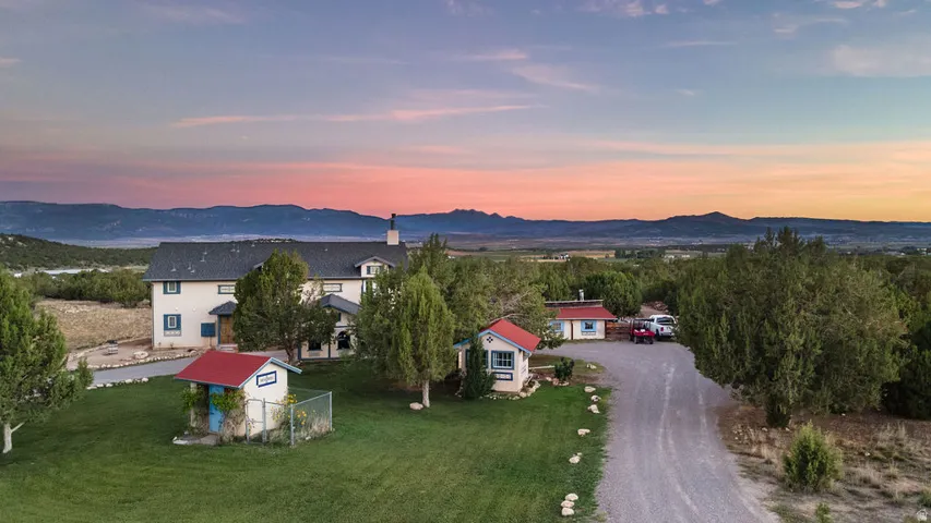 Expansive property featuring a gravel driveway, multiple outbuildings, mature trees, and a distant mountain range
