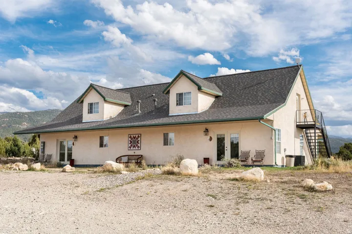Stucco exterior with dormer windows, dark asphalt shingle roof, and a visible exterior staircase