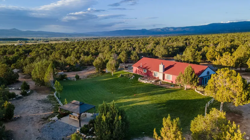 Expansive green lawn, surrounding mature trees, outdoor gazebo, distant mountain range, and a red-roofed residence