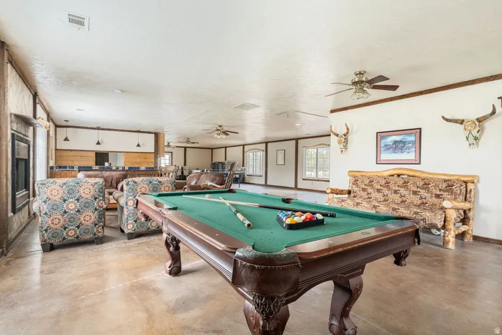 Spacious recreation room featuring a pool table, multiple windows, ceiling fans, and a built-in bar area with pendant lighting
