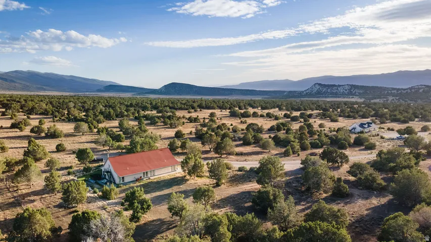 Expansive rural property featuring a single-story residence with a red roof, surrounded by numerous mature trees and natural landscaping