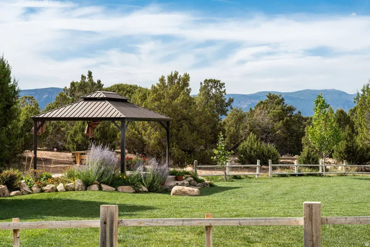 Expansive green lawn with a wooden split-rail fence, a metal gazebo, and surrounding mature trees