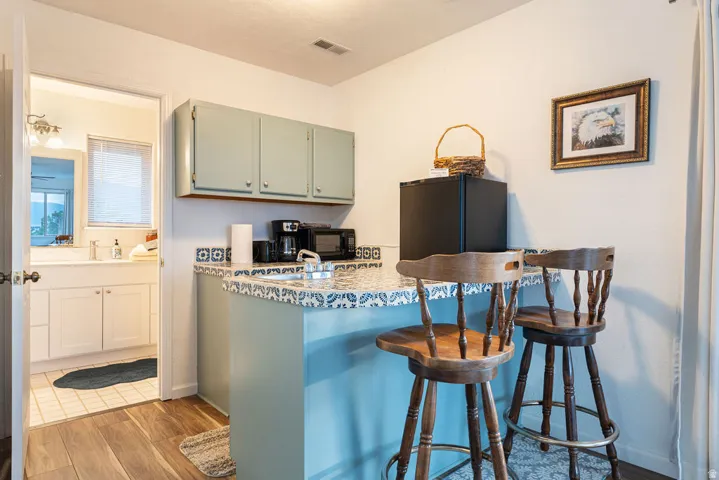 Wood-finish flooring leading to a built-in wet bar with a tiled countertop and overhead cabinetry