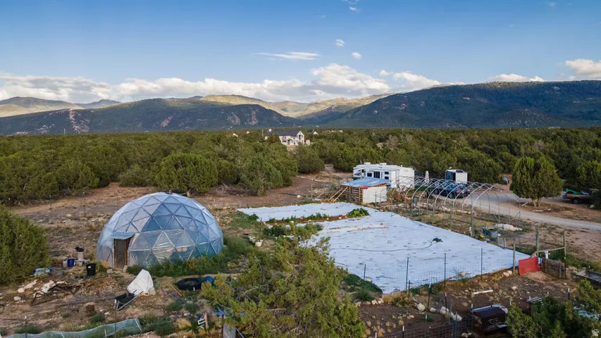 Geodesic dome structure, extensive open land, distant mountain range, dense tree line, and visible greenhouse framework