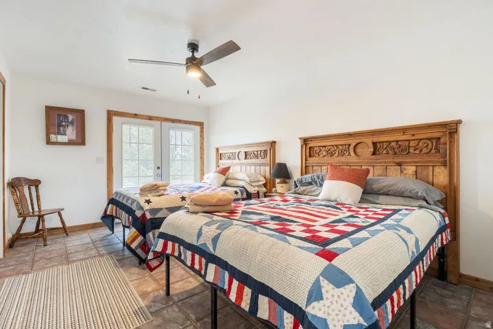 Two carved wood headboards, tile flooring, wood-framed double doors, and a ceiling fan with integrated lighting