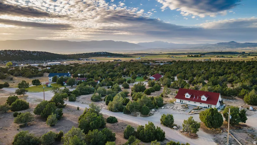 Expansive rural setting featuring a red-roofed residence with dormer windows, surrounded by numerous evergreen trees and a visible mountain range in the distance