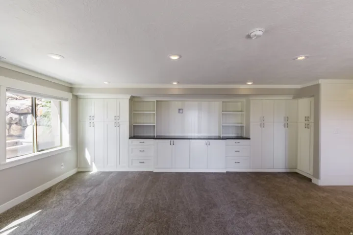 Built-in white cabinetry with dark countertops, recessed lighting, carpet flooring, a large window, and shiplap accent wall