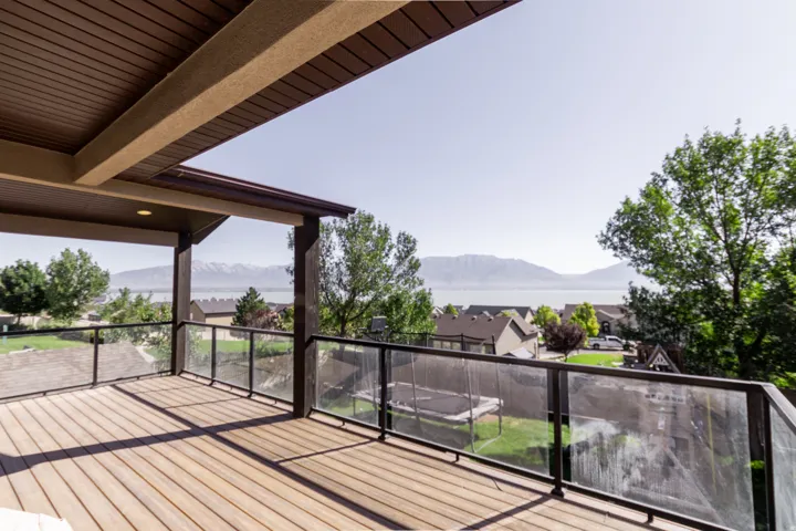 Expansive outdoor deck with wood-finish flooring, glass panel railing, and a covered ceiling
