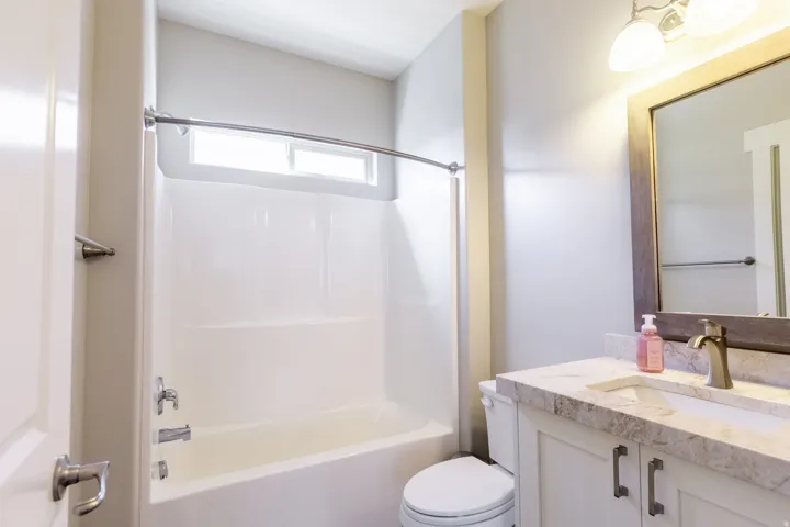Bathroom featuring a shower-tub combination, a vanity with a rectangular basin, a wall-mounted mirror with a wood-finish frame, and overhead vanity lighting