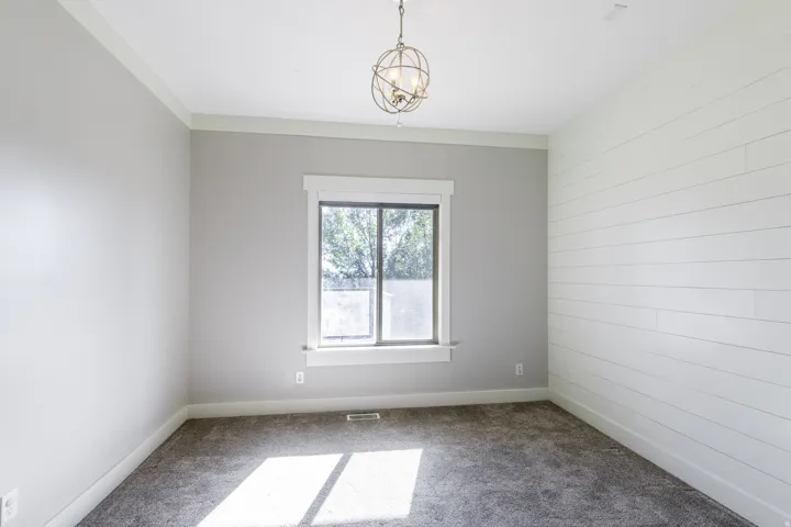 Textured carpet flooring, shiplap accent wall, crown molding, double-pane window, and a decorative ceiling light fixture