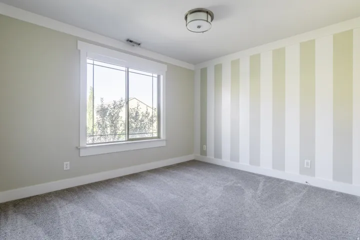Neutral wall tones, striped accent wall, window with white trim, flush mount ceiling light, and grey carpet flooring