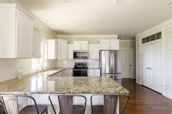 Kitchen featuring white cabinetry, stainless steel appliances, speckled stone countertops, and a subway tile backsplash