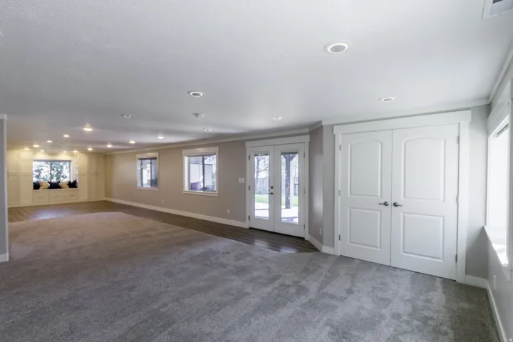 Recessed lighting, wood-finish flooring, light grey carpeting, built-in window seating with cabinetry, and double French doors with transom