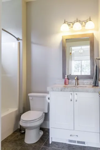 White vanity with chrome hardware, countertop, framed mirror, and three-light fixture