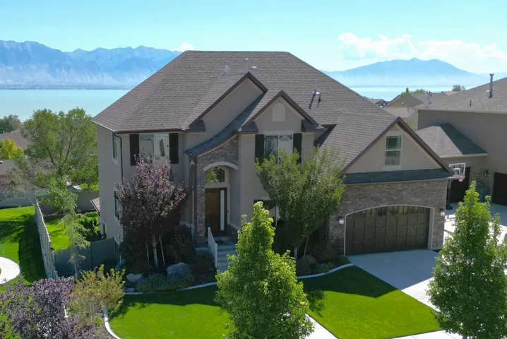 Two-story residence featuring a stone and stucco exterior, prominent gabled roofline, attached two-car garage with wood-finish door, and landscaped front yard with mature plantings