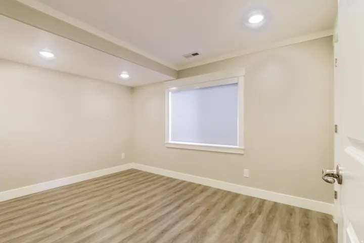 Recessed lighting, wood-finish flooring, white trim, and a single window